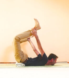 Die Yogastellung Dhanurasana mit einer Decke als Unterstützung für den Bewegungsansatz