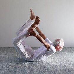 Fortgeschrittene Ausführung der Yogaübung Dhanurasana (Bogen): Der Übende hebt Brustkorb und Oberschenkel vom Boden und hält mit den Händen die Fußgelenke.